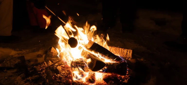 Sausage grilling over open fire on a barbecue, flames visible, outdoor cooking