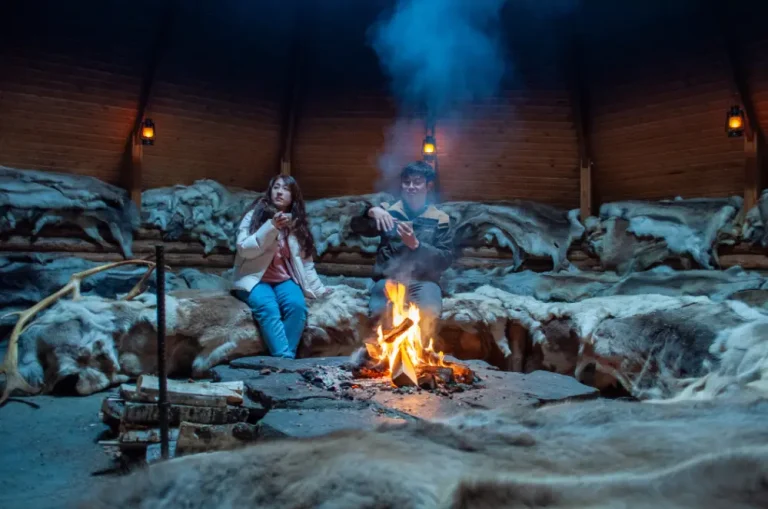 Guests listening stories around the fire about reindeer herding near Rovaniemi